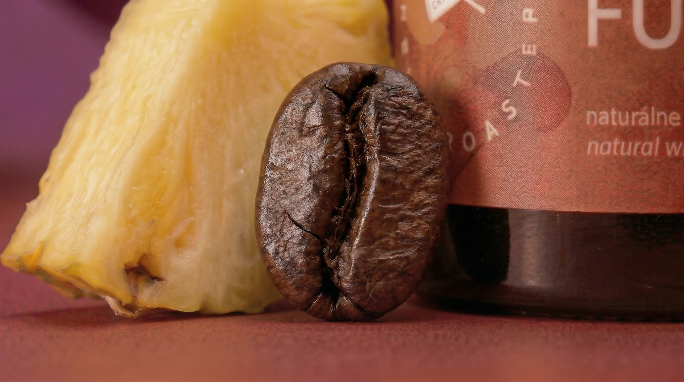 Extreme macro of a single coffee bean beside pineapple slice and jar label