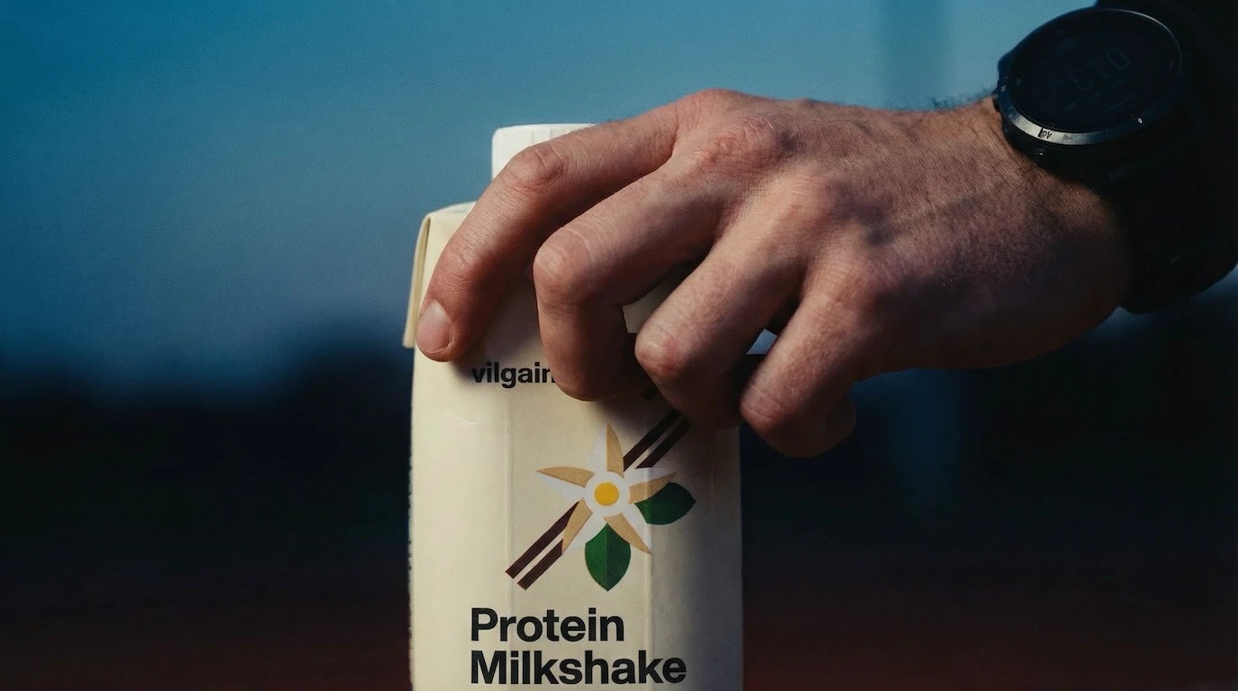 Hand holding Vilgain Protein Milkshake carton at outdoor dusk