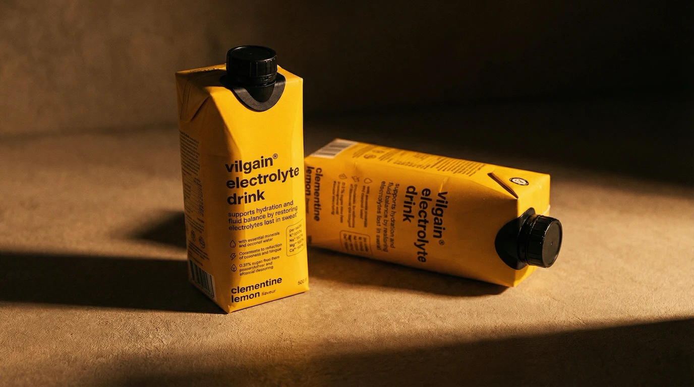 Two electrolyte drink cartons on sandy surface with hard shadows